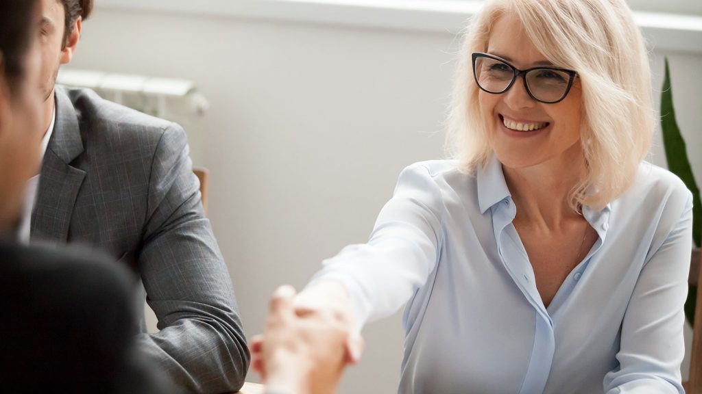 Two directors shake hands over a table in a boardroom in Norfolk, UK. They have benefitted from boardroom conflict resolution coaching.